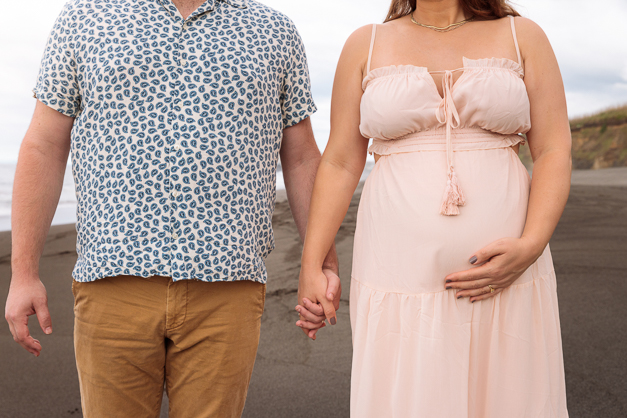 A couple holding hands while she touches her pregnant belly during a maternity session in the Azores