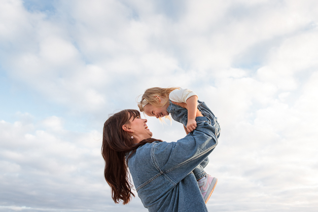 A woman playing with her daughter puting her up in the sky during a family photoshoot in the Azores