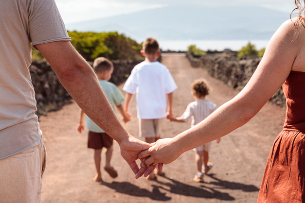 Mom and dad holds hands while their kids, in front of them appearing also holding hands during a family session in the Azores