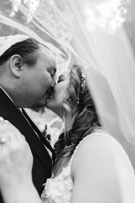 Black and white picture of bride and groom kissing udner the veil after the wedding