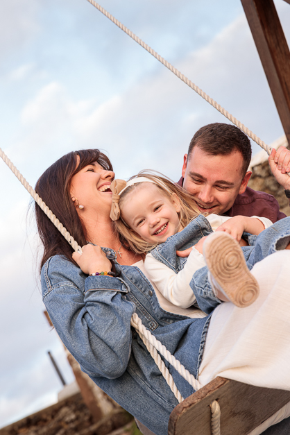 Family of three plays on a swing while smiling during a family session in the Azores