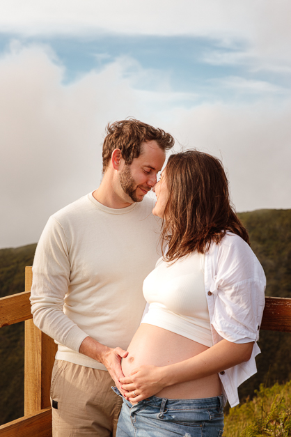 Couple looks at each other whiole both touch the girl's pregnant belly during a maternity session in the Azores