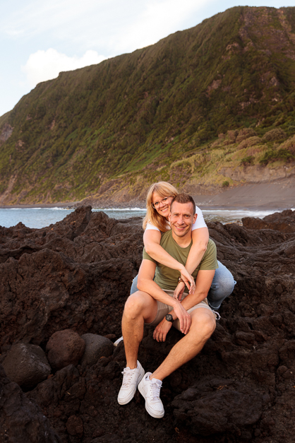 A guy and a girl lays on top of some volcanic stones in front of a beach during a couple session in the Azores
