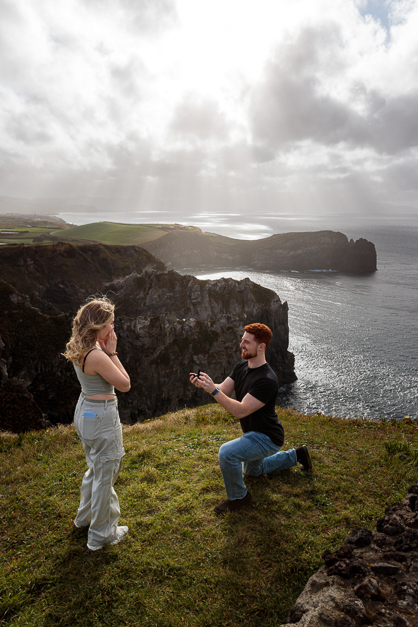 Moment of a surprise proposal in front of some dramatic cliffs during an engagement session in the island of Sao Miguel, in the Azores