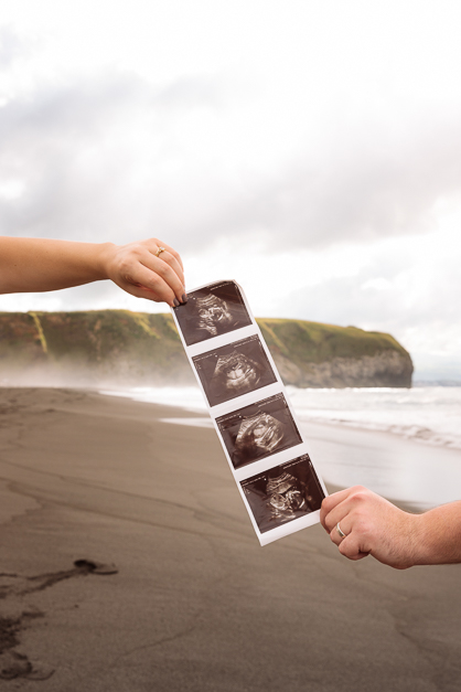 Ecography holded by both parents' hands in front of a beach landscape during a amternity photoshoot in the Azores