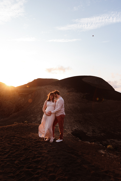 Guy and girld hold each other tight in front of a volcanic landcape during a pregnancy session in the Azores