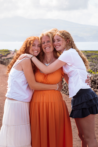 Two teenagers hug their mom while the three of them smile looking at the camera during a family session in the Azores