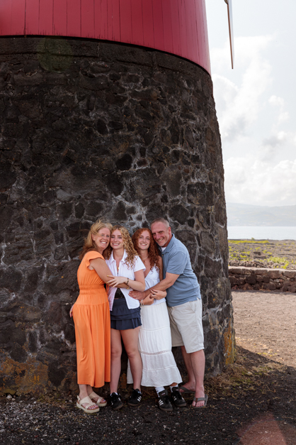 Family of four hugs in front of a wall made of volcanic stones during a family photoshoot in the Azores
