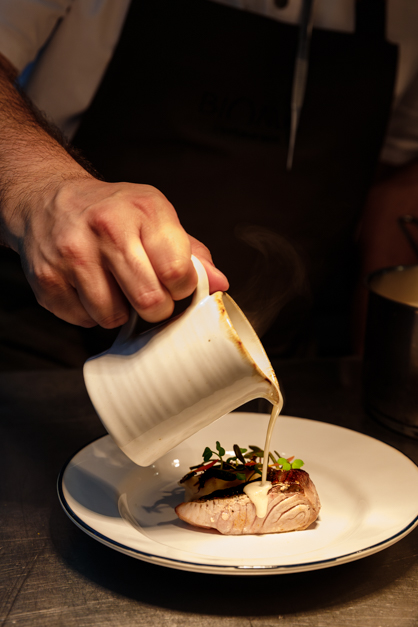 Hand serving the sauce over a fish dish during a restaurant service in the Azores