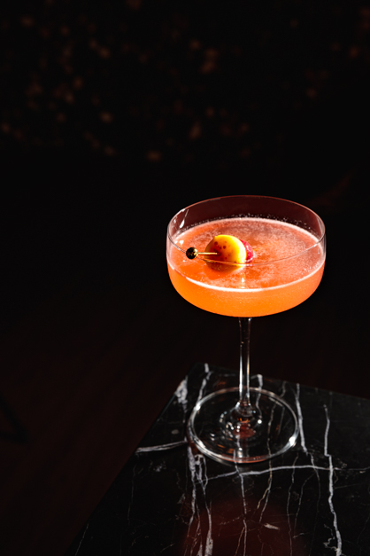 Cocktail lays on top of a dark table being the liwuid the only color of the image